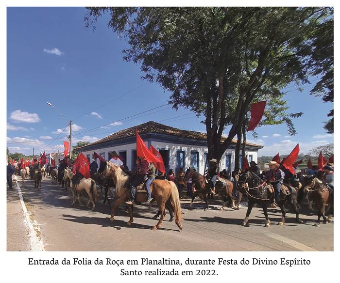 #pratodosverem:4 r- Entrada da Folia da Roça em Planaltina, durante Festa do Divino Espírito Santo realizada em 2022. Homens, mulheres e crianças estão montados em cavalos com bandeiras vermelhas erguidas. Ao centro algumas casas nas cores brancas e azuis com janelas diversas e telhas de cerâmica. Realização: Academia Planaltinense de Letras, Artes e Ciências (APLAC), pelo Ecomuseu Pedra Fundamental e pelo Coletivo Nativo Audiodescrição produzida  pelo Instituto de Promoção das Pessoas com Deficiência Visual Audiodescritora: Elma Lúcia Rodrigues Consultor: Fernando Rodrigues Este projeto é promovido com recursos do Fundo de Apoio a Cultura do DF